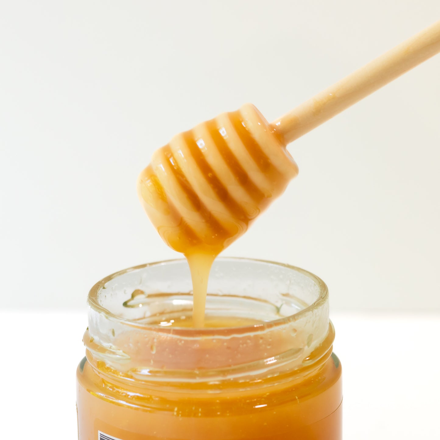 Honey dipper with honey dripping into a jar on a white background