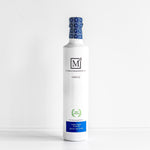 A 500mL glass bottle of Early Harvest Greek Extra Virgin Olive Oil with a blue and white label, cap with blue floral design, and the letter 'M' logo.