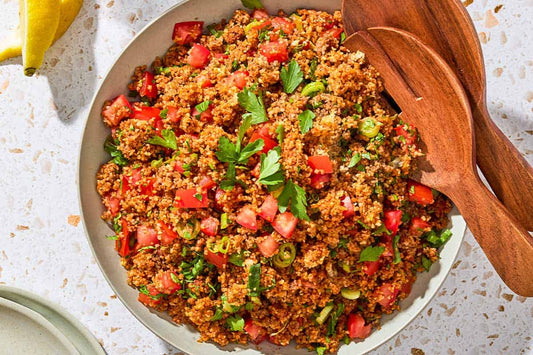 An overhead photo of kisir Turkish bulgur salad in a serving bowl with wooden serving utensils.
