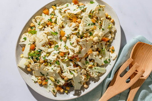 An overhead photo of a shaved cauliflower salad in a serving bowl next to a wooden serving fork.