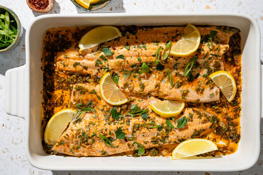 An overhead photo of baked trout garnished with parsley and green onions on a serving platter with lemon wedges.