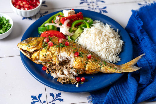 A serving of persian baked fish on a plate with rice and a salad. A part of the fish has been cut open showing the stuffing inside.