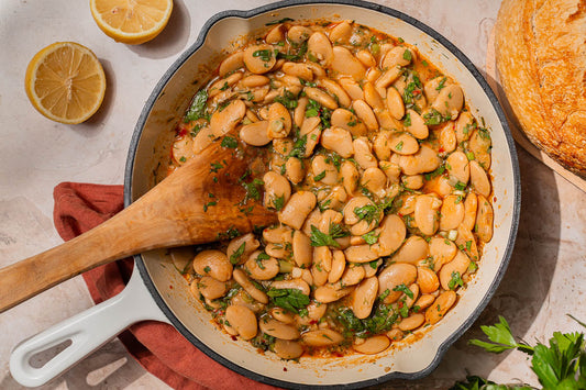 Serving of butter beans in a peach-colored bowl with a silver fork and a torn piece of crusty bread.