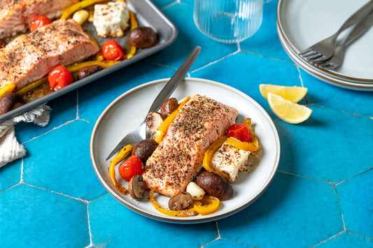 A close up of cooked baked salmon fillets with vegetables and feta on a sheet pan.