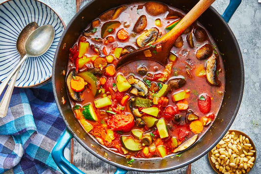 Steamy homemade vegetable soup in a dutch oven next to a wooden spoon.