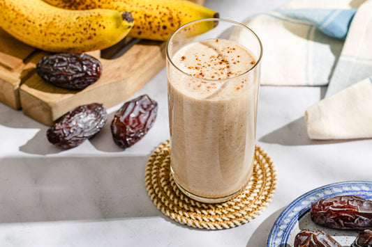 A glass cup filled with a tahini date shake with bananas and dates.