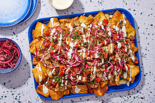 An overhead photo of a tray of pita chips covered in Mediterranean toppings.
