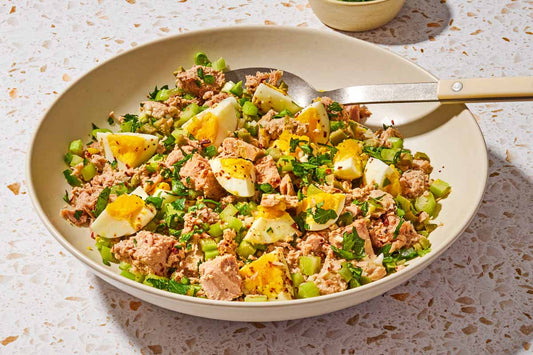A bowl with tuna, egg, and seasonings with a spoon.