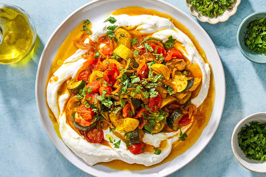 An overhead photo of a plate of garlic yogurt topped with zucchini, tomatoes, and seasoning.