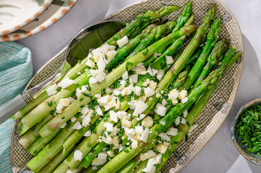 An overhead photo of a plate of asparagus garnished with chopped hard boiled eggs and seasonings.