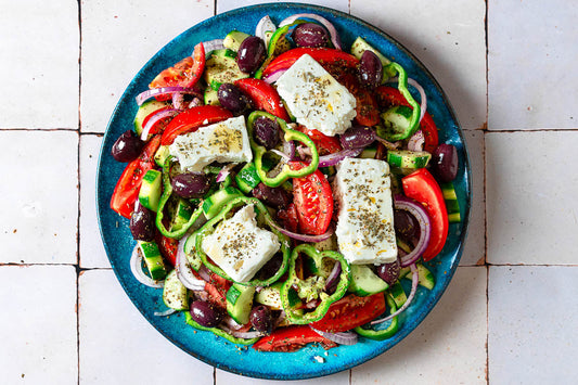 An overhead photo of a salad made with chopped vegetables and topped with cubes of feta and seasoning.
