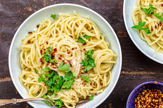 An overhead photo of a bowl of spaghetti pasta garnished with fresh herbs and seasonings.