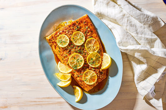 An overhead photo of a large filet of salmon garnished with seasoning and lemon slices.