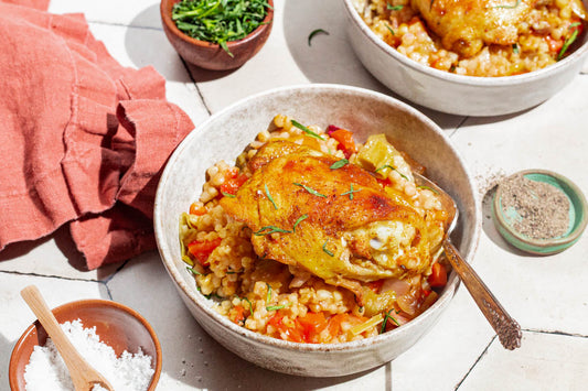 A bowl of couscous topped with a chicken thigh and fresh herbs.