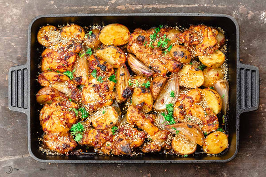 A baking tray filled with seasoned chicken thighs and garnished with fresh herbs.