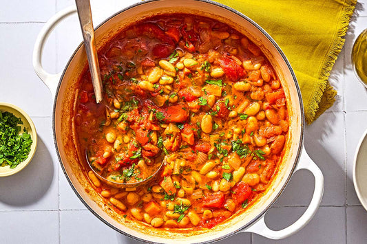 A large bowl of soup filled with red sauce, white beans, and fresh herbs.