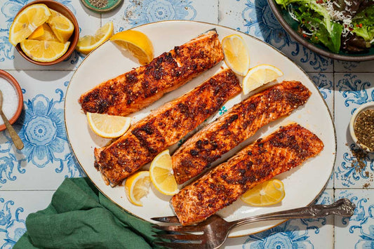 An overhead photo of 4 salmon filets on a plate garnished with lemon wedges.