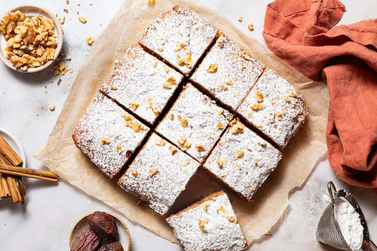 An overhead photo of a carrot cake sliced into 9 squares and topped with chopped nuts.
