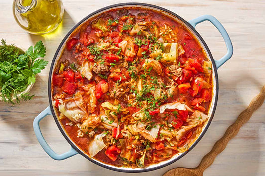 An overhead photo of a bot filled with cabbage, vegetables, and red sauce topped with fresh herbs.