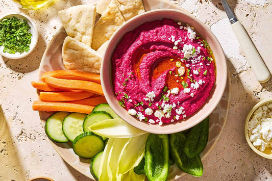 An overhead photo of beet hummus in a bowl with cut up vegetables and pita on a plate.