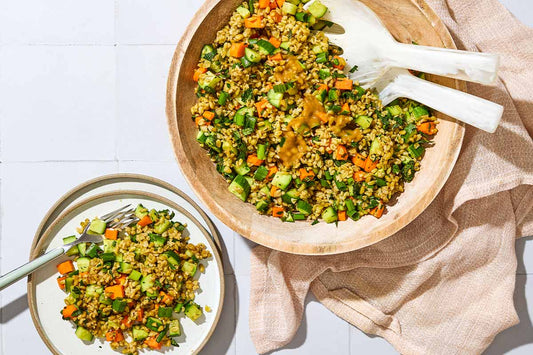 An overhead photo of a large bowl filled with freekeh salad and spoons with a side plate.