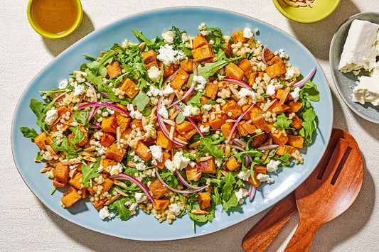 An overhead photo of a blue serving dish topped with fresh greens, sweet potato, and garnish.