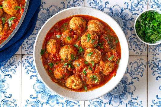 An overhead photo of a bowl of fish kofta in a red sauce and topped with fresh herbs.
