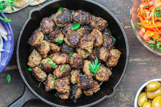 An overhead photo of a cast iron pan filled with meatballs and topped with fresh herbs.