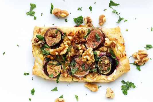 An overhead photo of a piece of flaky pastry topped with sliced figs, walnuts, and fresh herbs.