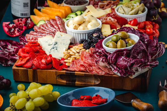 A wooden board topped with charcuterie with fruit, olives, cured meats, and cheese.
