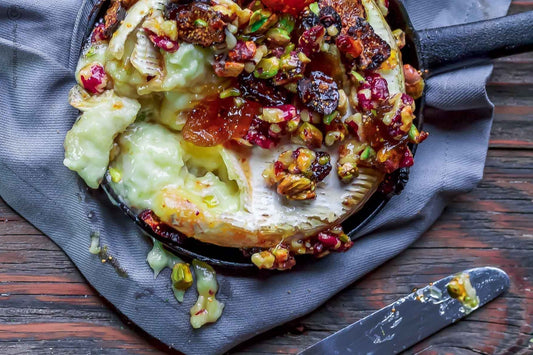 An overhead photo of a cast iron dish filled with melted baked brie topped with fig jam and nuts.