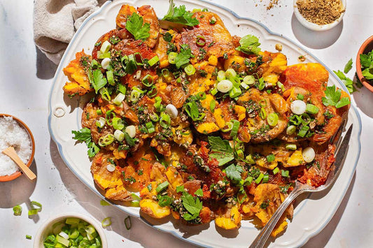 An overhead photo of a long plate topped with smashed potatoes and topped with fresh herbs and seasoning.