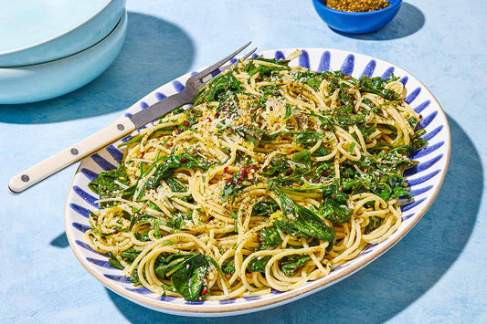 A blue and white serving dish topped with spaghetti, spinach, and fresh herbs.