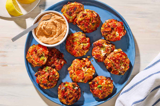 An overhead photo of twelve tomato fritters on top of a blue plate with a bowl of yogurt dip.
