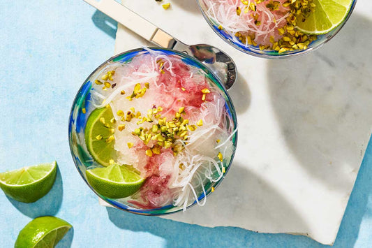 An overhead photo of a bowl with rose and lime granita and topped with lime wedges.
