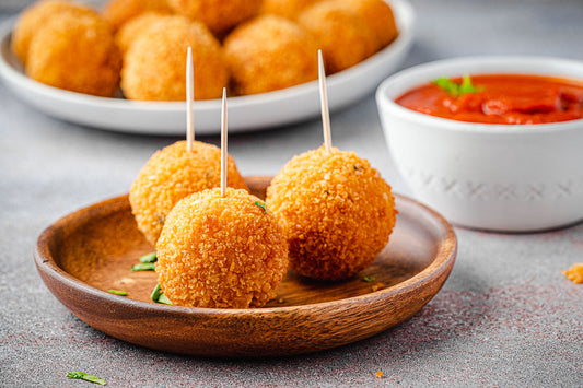 A small plate with three arancini balls next to a bowl of red dipping sauce.