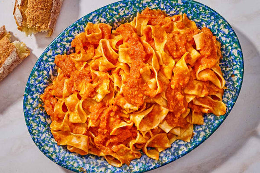 A blue serving dish topped with a large serving of pasta in a red lentil bolognese sauce.