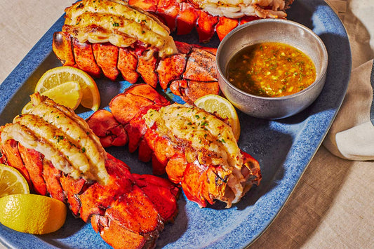 A close up of three lobster tails garnished with lemon wedges and a bowl of dipping sauce.