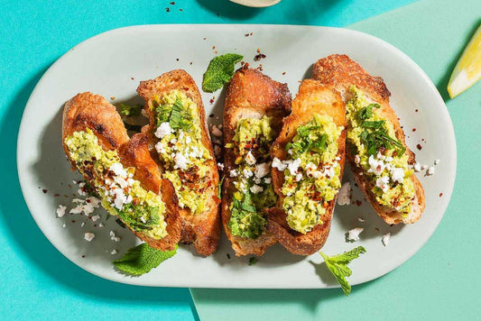 An overhead photo of a serving plate with 5 crostini topped with smashed peas and fresh herbs.