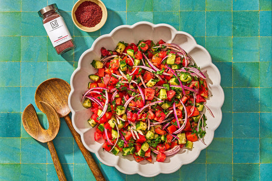 An overhead photo of a serving bowl filled with chopped cucumber, tomato, and red onions. 