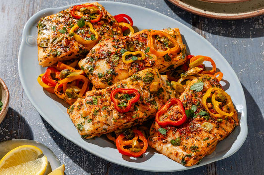 A serving dish topped with 4 baked haddock filets and topped with sliced peppers and fresh herbs.