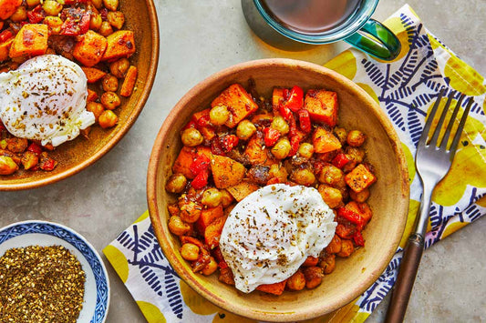 An overhead photo of two bowls of chopped sweet potatoes and chickpeas topped with a poached egg and seasoning.