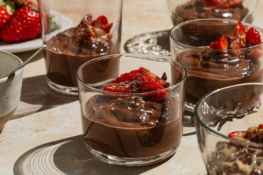 Multiple glass cups filled with chocolate pudding and topped with fresh strawberries.
