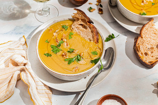 A bowl of acorn squash soup topped with fresh herbs with a spoon and fresh sliced bread.