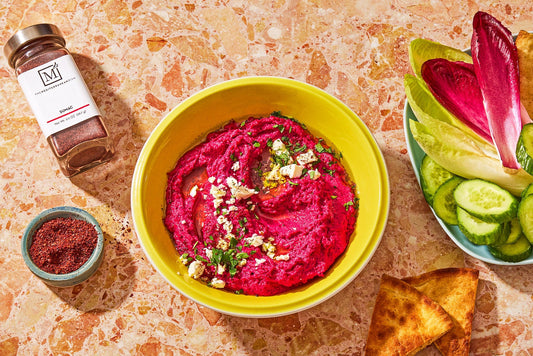 An overhead photo of beet hummus in a bowl with cut up vegetables and pita on a plate.