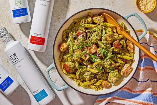A white bowl filled with pasta in a creamy pesto sauce and chicken with a fresh basil garnish and a bowl of red pepper flakes on the side.