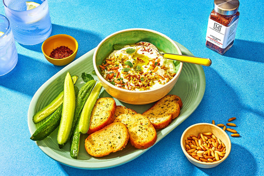 An overhead photo of a serving dish filled with whipped feta dip topped with olive oil and fresh herbs and slices of pita bread.