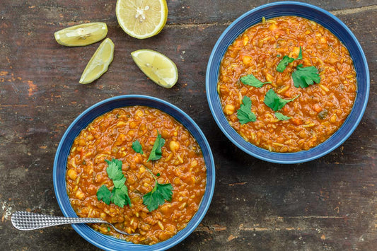 An overhead photo of two bowls of lentil and chickpea soup with lemon wedges on the side.