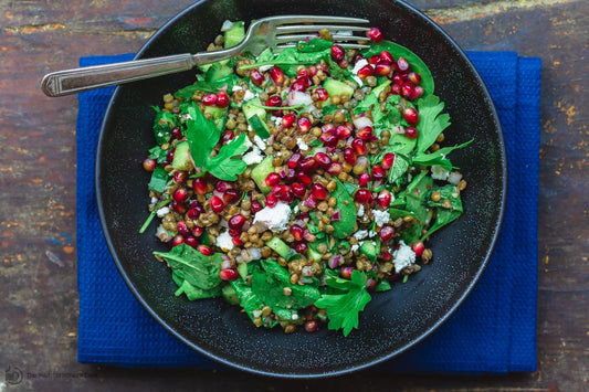An overhead photo of a bowl of greens topped with lentils, pomegranate seeds, and feta cheese on top of a blue napkin.