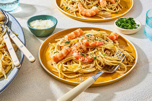 A plate topped with cacio e pepe spaghetti and topped with shrimp and fresh herbs.
